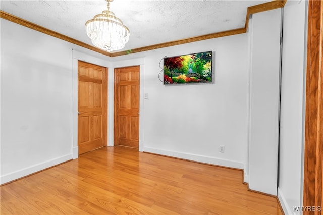 spare room featuring ornamental molding, light hardwood / wood-style floors, a textured ceiling, and a notable chandelier