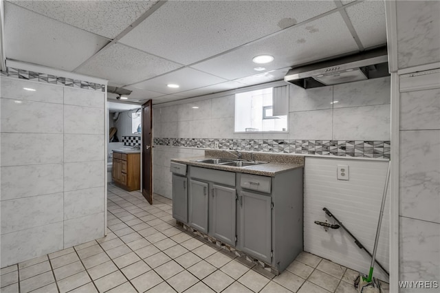 kitchen featuring gray cabinets, a paneled ceiling, sink, tile walls, and wall chimney exhaust hood