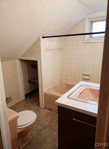 full bathroom with vaulted ceiling, tile patterned floors, toilet, vanity, and tiled shower / bath combo