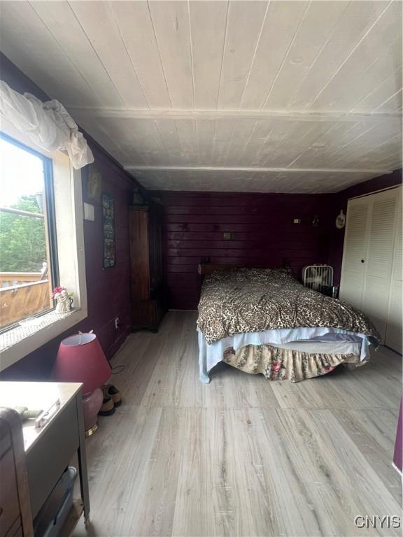 bedroom with wood walls, wooden ceiling, and light wood-type flooring