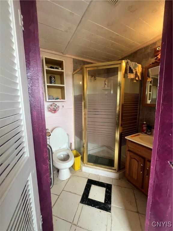 bathroom with an enclosed shower, vanity, tile walls, and toilet