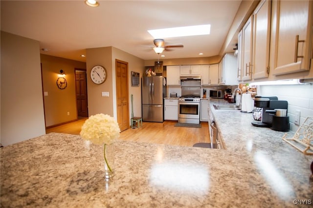 kitchen featuring sink, a skylight, light hardwood / wood-style flooring, appliances with stainless steel finishes, and ceiling fan