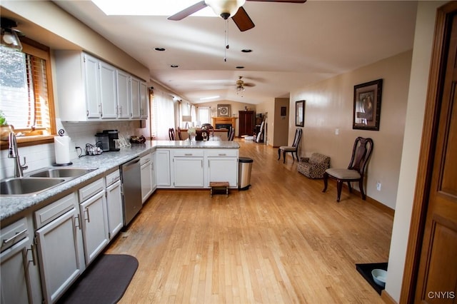 kitchen featuring lofted ceiling, sink, stainless steel dishwasher, kitchen peninsula, and white cabinets