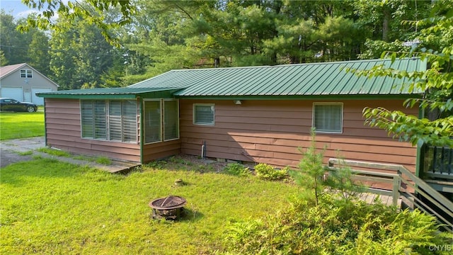 back of house featuring a fire pit, metal roof, and a lawn