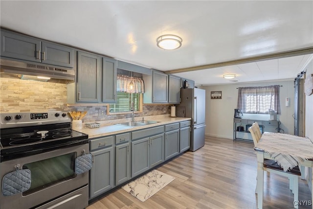 kitchen with stainless steel electric range oven, freestanding refrigerator, gray cabinetry, under cabinet range hood, and a sink