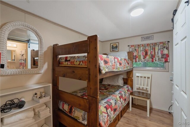 bedroom with ornamental molding, light wood-type flooring, and a barn door