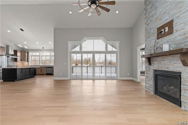 unfurnished living room featuring light wood-type flooring, ceiling fan, a fireplace, a towering ceiling, and sink