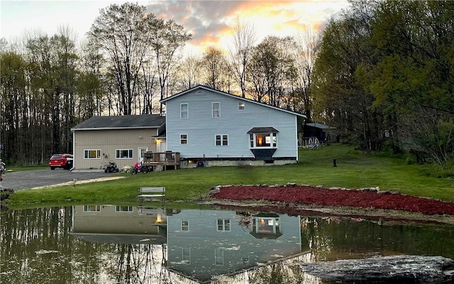 back house at dusk with a water view and a yard