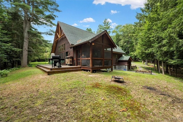 rear view of house featuring a lawn, a fire pit, a sunroom, and a wooden deck