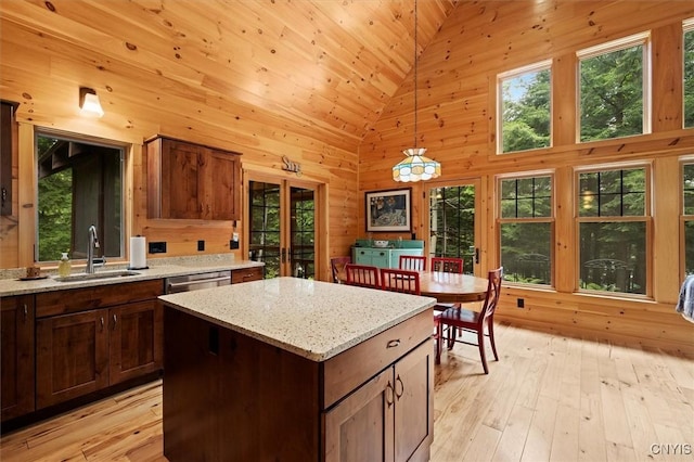 kitchen featuring sink, decorative light fixtures, a center island, light stone countertops, and high vaulted ceiling