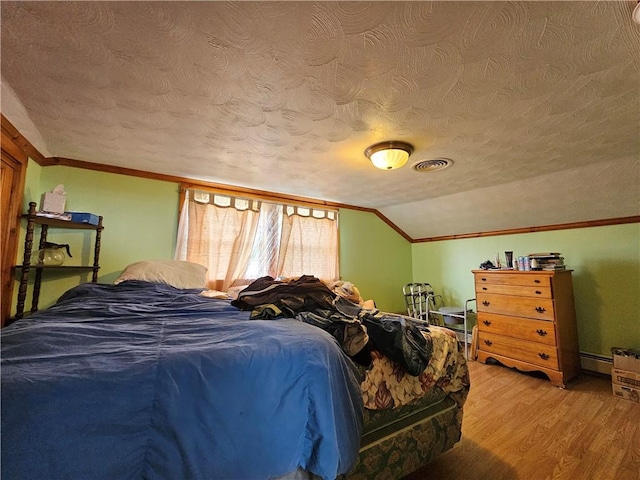 bedroom with a textured ceiling, light wood-style flooring, crown molding, baseboard heating, and lofted ceiling