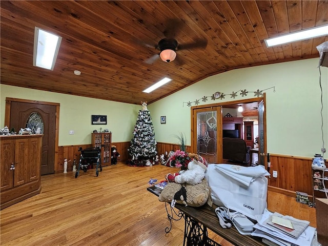 dining area with wainscoting, ceiling fan, vaulted ceiling with skylight, light wood-type flooring, and wooden ceiling