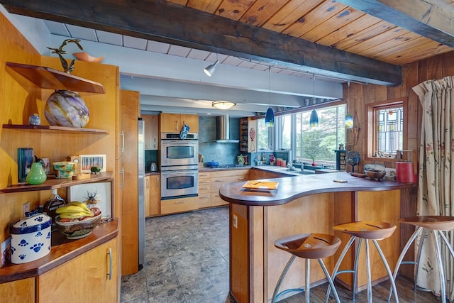 kitchen with wood walls, wall chimney range hood, a breakfast bar, kitchen peninsula, and double oven