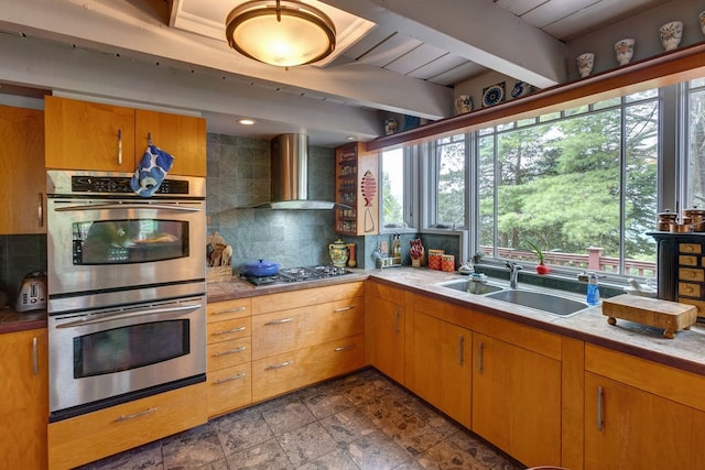 kitchen with beamed ceiling, sink, wall chimney exhaust hood, stainless steel appliances, and decorative backsplash