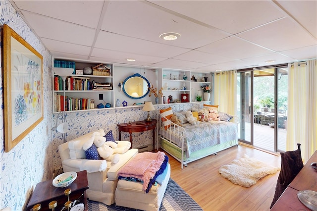 bedroom featuring a drop ceiling, access to exterior, expansive windows, and wood-type flooring