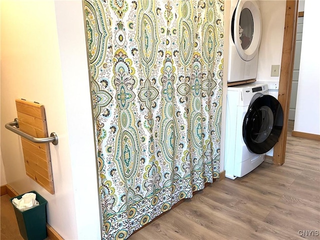 clothes washing area with baseboards, wood finished floors, laundry area, and stacked washer / dryer