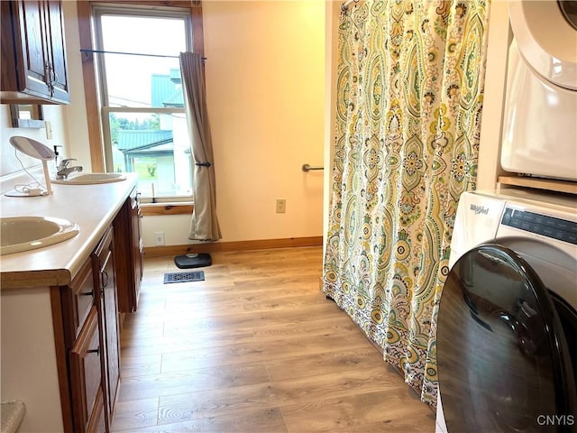 full bathroom featuring baseboards, double vanity, stacked washer and clothes dryer, wood finished floors, and a sink