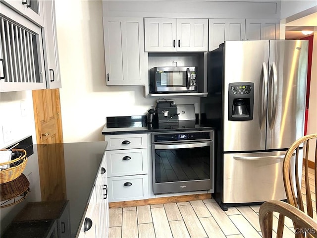 kitchen with dark countertops, white cabinets, stainless steel appliances, and wood tiled floor