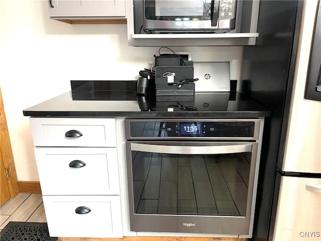kitchen with dark countertops, white cabinets, light wood-type flooring, and stainless steel appliances
