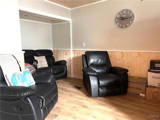 living room featuring visible vents, a wainscoted wall, wood walls, ornamental molding, and wood finished floors