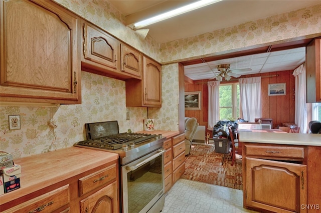 kitchen featuring wood walls, ceiling fan, light tile patterned floors, and gas range