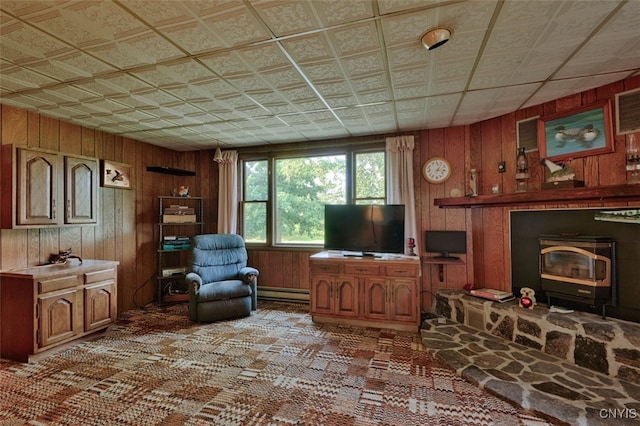 living room featuring a wood stove, a baseboard heating unit, and wood walls