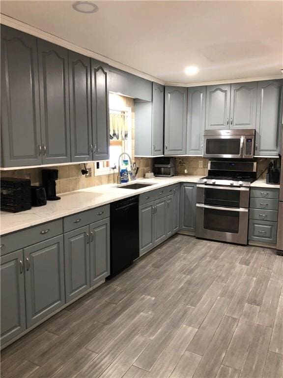 kitchen with gray cabinets, decorative backsplash, appliances with stainless steel finishes, a sink, and wood finished floors