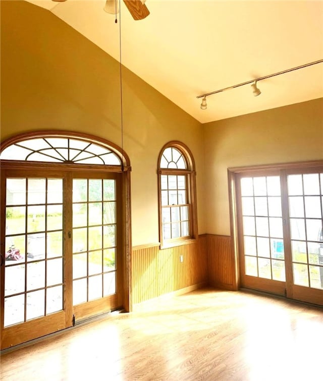 unfurnished room with a wainscoted wall, vaulted ceiling, wood finished floors, and a wealth of natural light