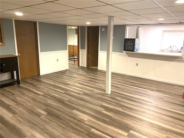 finished basement featuring a wainscoted wall, baseboards, a drop ceiling, and wood finished floors