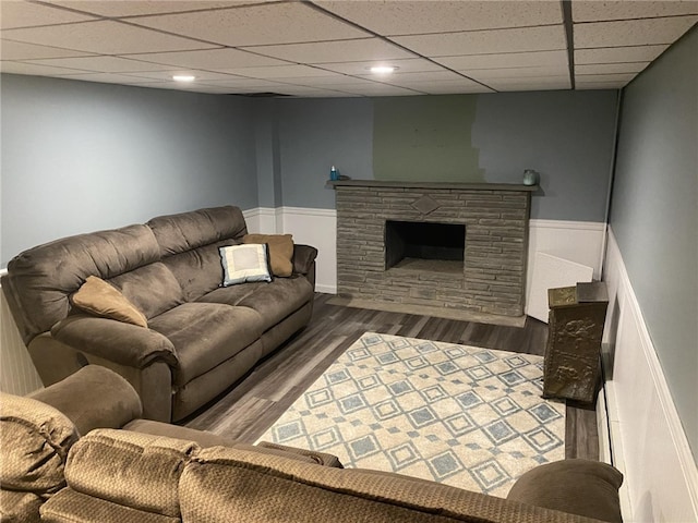 living room featuring a paneled ceiling, a wainscoted wall, wood finished floors, and a stone fireplace