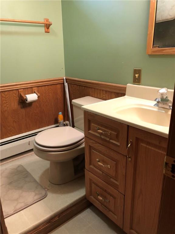 half bathroom featuring toilet, wooden walls, a wainscoted wall, vanity, and baseboard heating