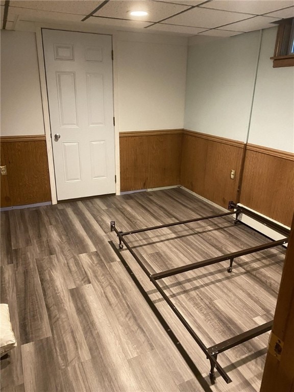 unfurnished bedroom featuring a paneled ceiling, a wainscoted wall, wood walls, and wood finished floors