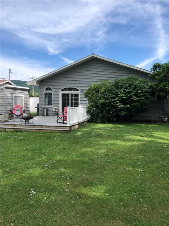 rear view of property featuring a yard, a shed, a deck, and an outbuilding