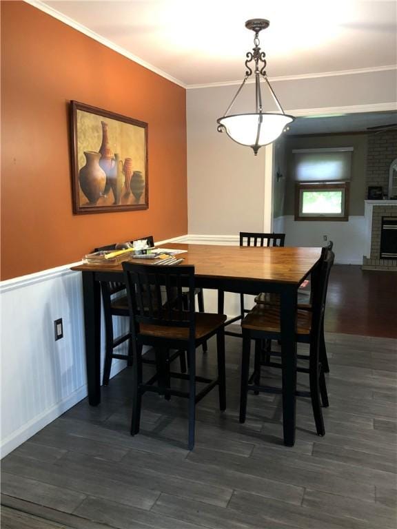 dining room with a brick fireplace, ornamental molding, dark wood-style flooring, and wainscoting