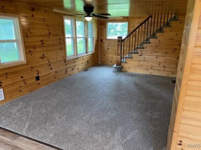 unfurnished living room with carpet, wooden walls, and ceiling fan