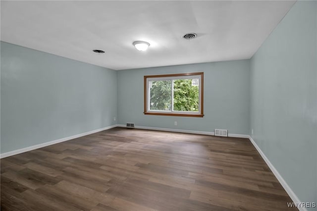 spare room featuring dark wood-style floors, visible vents, and baseboards