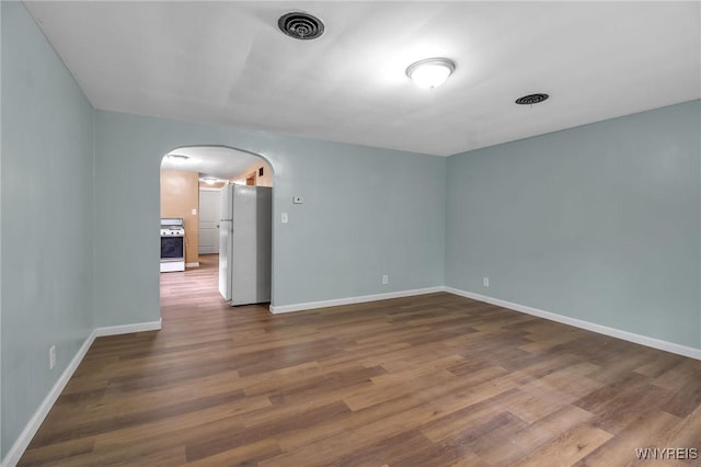 spare room featuring visible vents, arched walkways, dark wood-style flooring, and baseboards