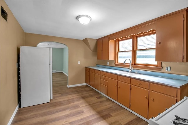 kitchen with light countertops, light wood-style floors, arched walkways, and a sink