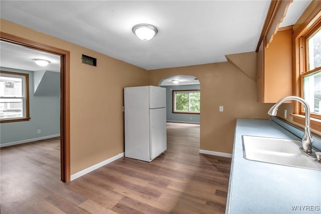 kitchen featuring wood finished floors, baseboards, arched walkways, freestanding refrigerator, and a sink