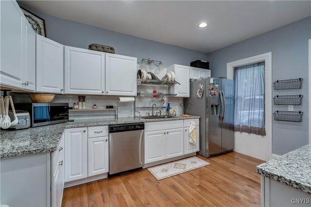 kitchen featuring appliances with stainless steel finishes, white cabinetry, sink, light stone countertops, and light hardwood / wood-style flooring