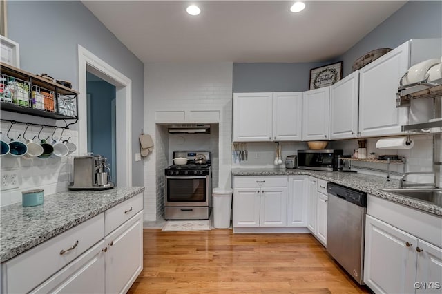 kitchen with white cabinetry, decorative backsplash, light stone counters, stainless steel appliances, and light wood-type flooring