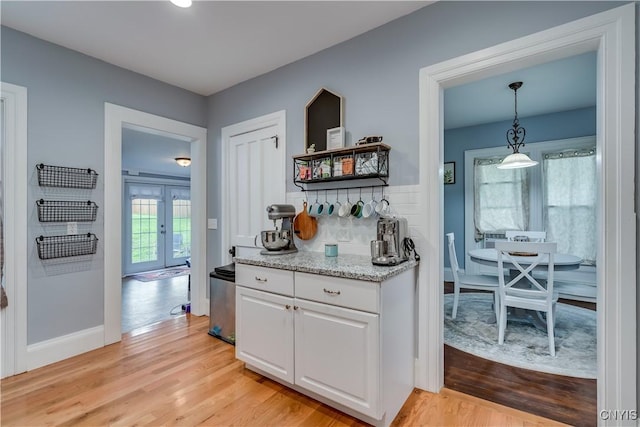 kitchen with tasteful backsplash, white cabinetry, light wood-type flooring, and decorative light fixtures