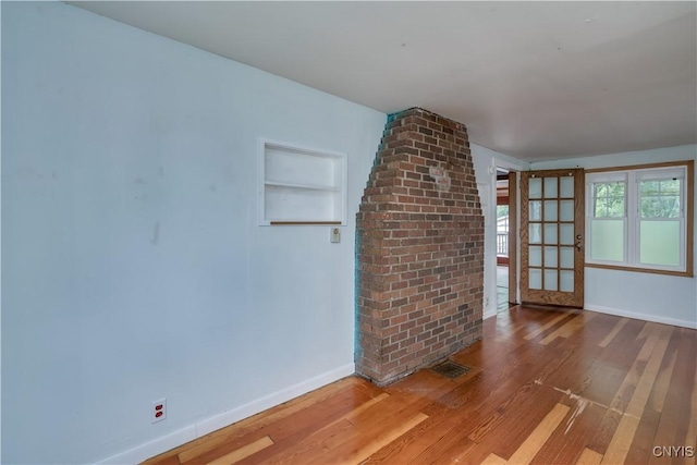 unfurnished living room featuring hardwood / wood-style flooring and built in shelves