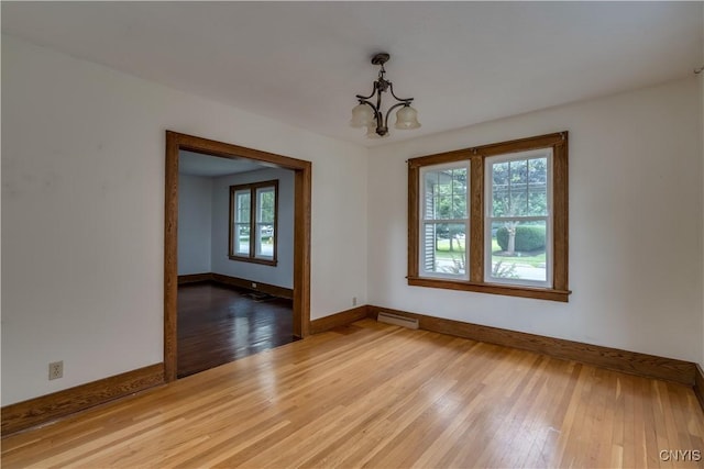 spare room with a chandelier, light hardwood / wood-style flooring, and a baseboard heating unit