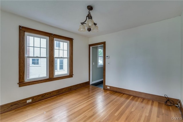 unfurnished room with plenty of natural light, a chandelier, and light hardwood / wood-style floors