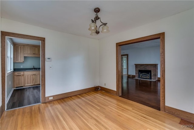 spare room featuring sink, a fireplace, an inviting chandelier, and light hardwood / wood-style flooring