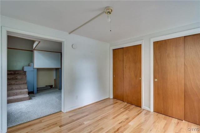 unfurnished bedroom with multiple closets, ceiling fan, and light hardwood / wood-style flooring