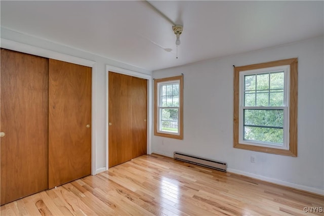 unfurnished bedroom featuring multiple closets, ceiling fan, baseboard heating, and light hardwood / wood-style floors