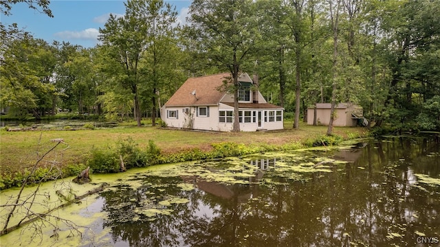 rear view of property featuring a water view, a lawn, and an outbuilding