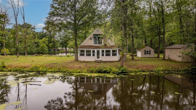 back of property featuring a water view, a lawn, and an outbuilding